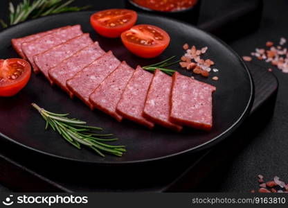 Delicious fresh sausage salami with salt, tomatoes and spices on a dark concrete background