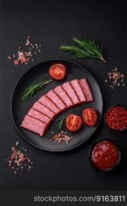 Delicious fresh sausage salami with salt, tomatoes and spices on a dark concrete background
