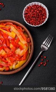 Delicious fresh saute sweet bell pepper slices with onion, salt, spices and herbs on a dark concrete background