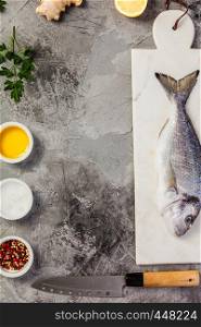 Delicious fresh sea bream fish on marble board, herbs and spices over grey stone background. Cooking concept, copyspace. Delicious fresh sea bream fish, flat lay, top view