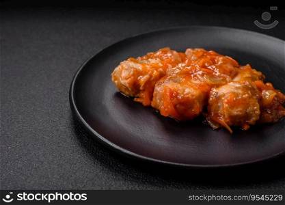 Delicious fresh sea fish cut into pieces and baked in tomato sauce with salt, spices and herbs on a dark concrete background