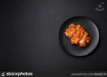 Delicious fresh sea fish cut into pieces and baked in tomato sauce with salt, spices and herbs on a dark concrete background