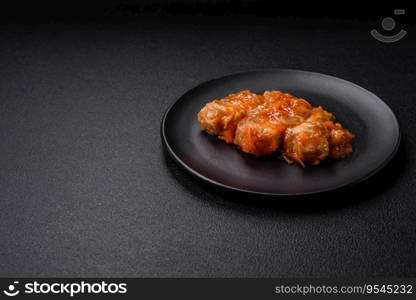 Delicious fresh sea fish cut into pieces and baked in tomato sauce with salt, spices and herbs on a dark concrete background