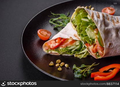 Delicious fresh shawarma with tomatoes, peppers, cucumber and sauces on a dark concrete background. Fast food