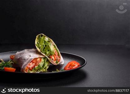 Delicious fresh shawarma with tomatoes, peppers, cucumber and sauces on a dark concrete background. Fast food
