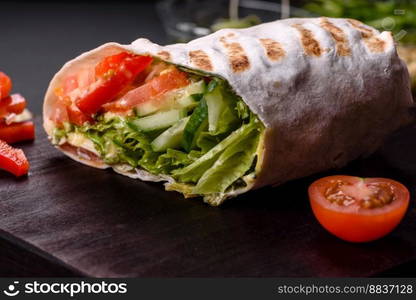 Delicious fresh shawarma with tomatoes, peppers, cucumber and sauces on a dark concrete background. Fast food