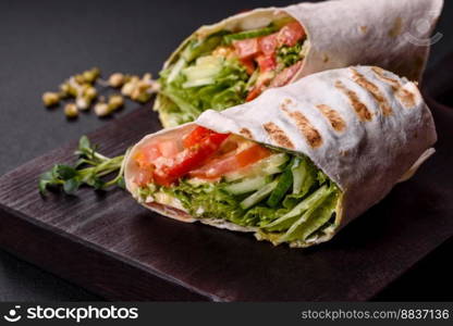 Delicious fresh shawarma with tomatoes, peppers, cucumber and sauces on a dark concrete background. Fast food