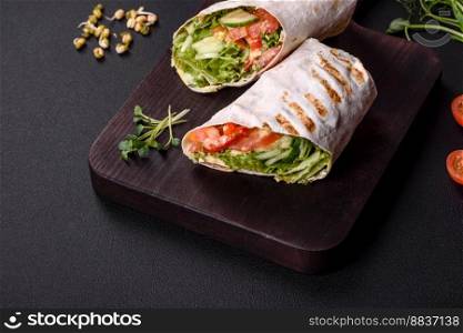 Delicious fresh shawarma with tomatoes, peppers, cucumber and sauces on a dark concrete background. Fast food