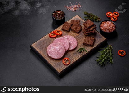 Delicious fresh smoked sausage cut with slices on a wooden cutting board against a dark concrete background. Delicious fresh smoked sausage cut with slices on a wooden cutting board