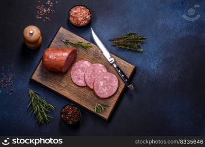 Delicious fresh smoked sausage cut with slices on a wooden cutting board against a dark concrete background. Delicious fresh smoked sausage cut with slices on a wooden cutting board