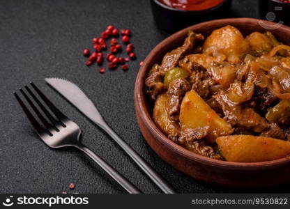 Delicious fresh stew of potatoes, tomatoes, onions, carrots and beef meat with salt, spices and herbs on a dark concrete background