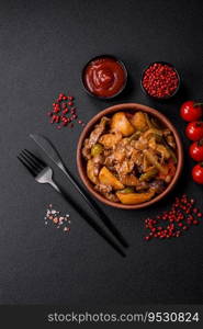 Delicious fresh stew of potatoes, tomatoes, onions, carrots and beef meat with salt, spices and herbs on a dark concrete background