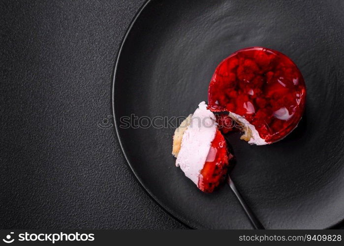 Delicious fresh sweet cheesecake cake with berries and red color jelly on a dark concrete background