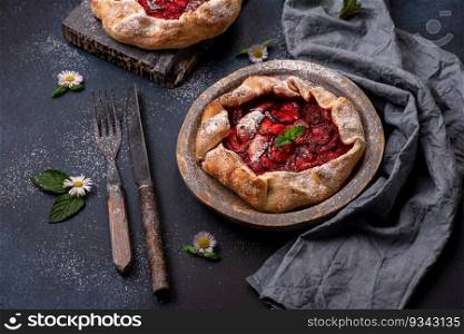Delicious fresh sweet homemade rustic style strawberry tart with wild flowers on dark textured background