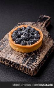 Delicious fresh sweet round tart with ripe blueberries and cream on a dark concrete background