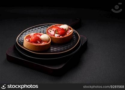 Delicious fresh sweet tartlets with strawberries and coconut flakes on a dark concrete background