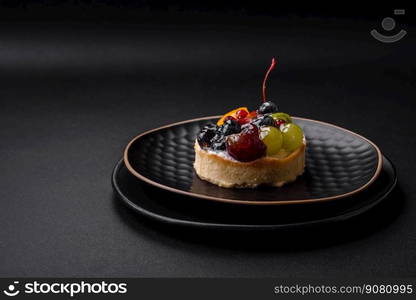 Delicious fresh tart with blueberries, cherries, grapes on a black ceramic plate on a dark concrete background