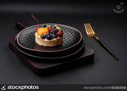 Delicious fresh tart with blueberries, cherries, grapes on a black ceramic plate on a dark concrete background
