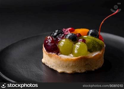 Delicious fresh tart with blueberries, cherries, grapes on a black ceramic plate on a dark concrete background