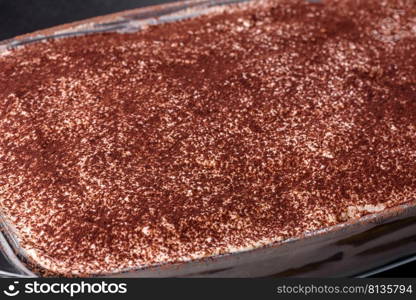 Delicious fresh tiramisu cake in a glass rectangular shape against a dark concrete background. Making sweets at home. Delicious fresh tiramisu cake in a glass rectangular shape