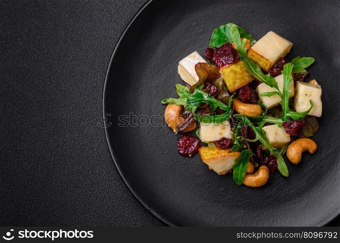 Delicious fresh vegan salad with pear, brie cheese, nuts and grains, and arugula on a ceramic plate on a dark background