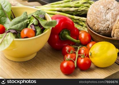 Delicious fresh vegetables for dinner standing ready to prepare on a kitchen counter with ripe cherry tomatoes, red bell pepper, lemon, asparagus spears, baby spinach and brown bread rolls