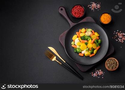 Delicious fresh vegetables steamed carrots, broccoli, cauliflower on a black plate on a dark concrete background