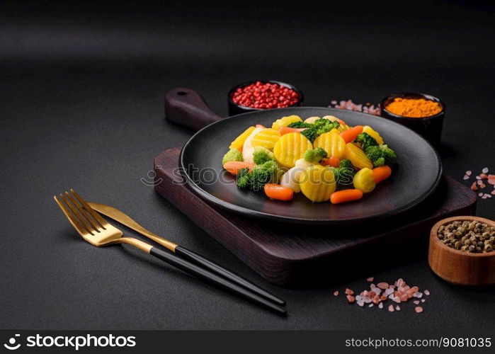 Delicious fresh vegetables steamed carrots, broccoli, cauliflower on a black plate on a dark concrete background