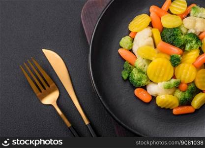 Delicious fresh vegetables steamed carrots, broccoli, cauliflower on a black plate on a dark concrete background