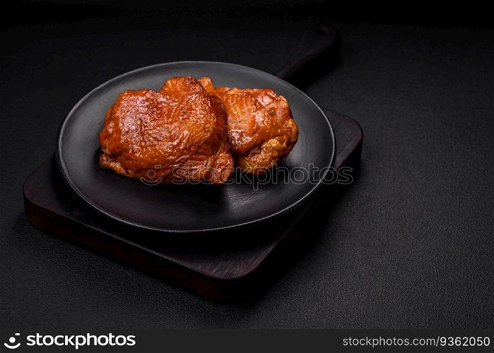 Delicious fried or smoked chicken thighs grilled with spices and herbs on a dark concrete background