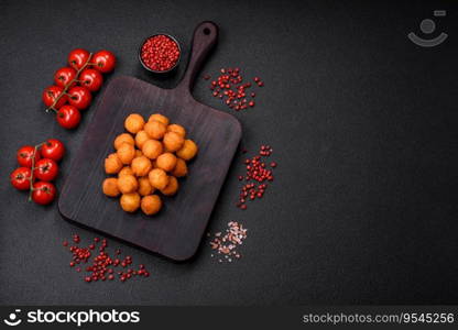 Delicious fried potato balls with breaded mozzarella, salt, spices and herbs on a dark concrete background