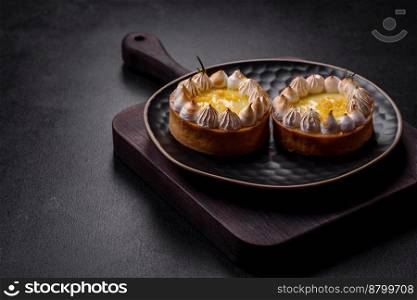 Delicious fruity sweet tart with lemon flavor and cream on a black plate on a dark concrete background