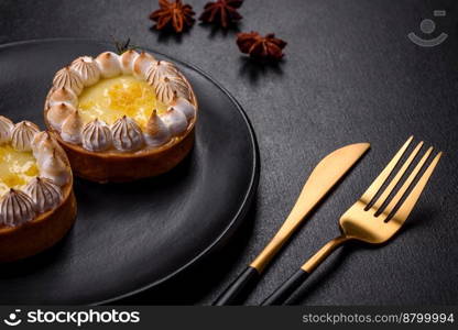 Delicious fruity sweet tart with lemon flavor and cream on a black plate on a dark concrete background