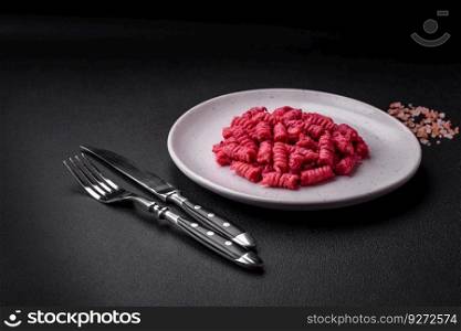 Delicious fusilli pasta with beetroot pesto, parmesan, salt and spices on a dark concrete background