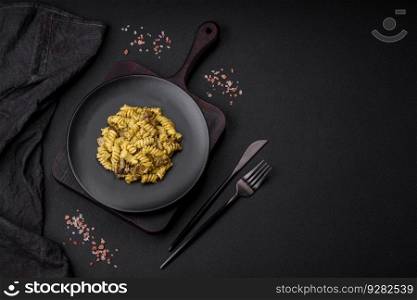 Delicious fusilli pasta with green pesto sauce, with salt and spices on a ceramic plate on a dark concrete background