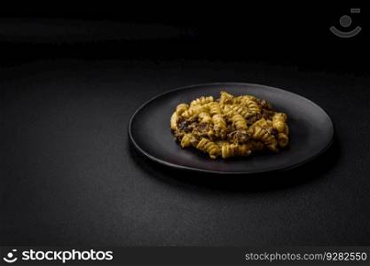 Delicious fusilli pasta with green pesto sauce, with salt and spices on a ceramic plate on a dark concrete background