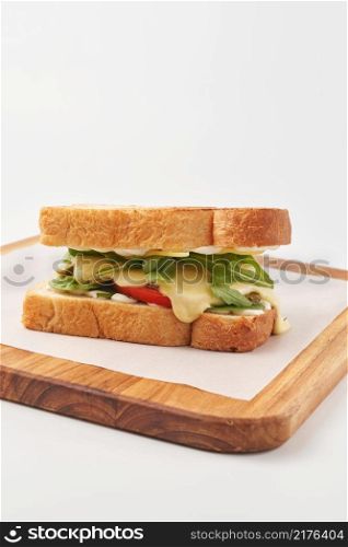 Delicious golden toasted bread of sandwich stuffed with green arugula leaves and vegetables with melted cheese and served on wooden board with paper. Healthy breakfast sandwich on board