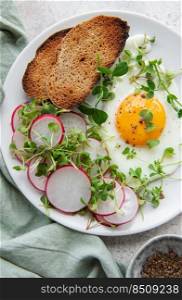 Delicious gourmet Breakfast. Rye bread  with fried egg,  freshly ground pepper and salad with redish and microgreens. Healthy food. 