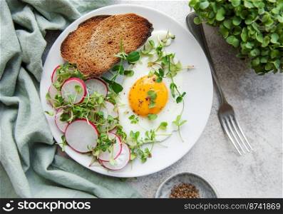 Delicious gourmet Breakfast. Rye bread  with fried egg,  freshly ground pepper and salad with redish and microgreens. Healthy food. 