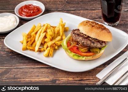 Delicious grilled burger on white plate on wooden table. With sauces and french fries