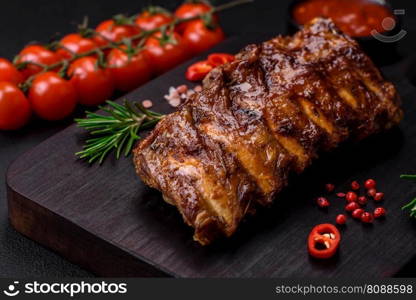 Delicious grilled pork ribs with sauce, spices and herbs on a dark concrete background