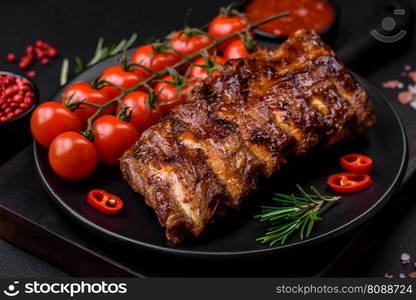 Delicious grilled pork ribs with sauce, spices and herbs on a dark concrete background