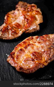 Delicious grilled pork steak on a stone board. On a black background. High quality photo. Delicious grilled pork steak on a stone board.