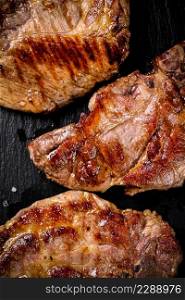 Delicious grilled pork steak on a stone board. On a black background. High quality photo. Delicious grilled pork steak on a stone board.