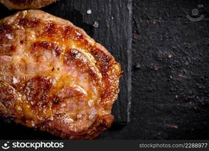 Delicious grilled pork steak on a stone board. On a black background. High quality photo. Delicious grilled pork steak on a stone board. 