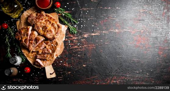Delicious grilled pork steak with tomato sauce and rosemary. Against a dark background. High quality photo. Delicious grilled pork steak with tomato sauce and rosemary.