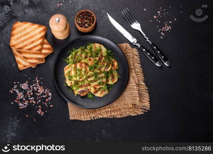 Delicious grilled potato slices with spices and herbs on a black plate against a dark concrete background. Cooking at home. Delicious grilled potato slices with spices and herbs on a black plate