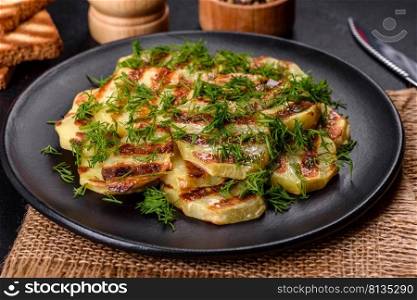 Delicious grilled potato slices with spices and herbs on a black plate against a dark concrete background. Cooking at home. Delicious grilled potato slices with spices and herbs on a black plate