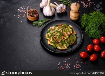 Delicious grilled potato slices with spices and herbs on a black plate against a dark concrete background. Cooking at home. Delicious grilled potato slices with spices and herbs on a black plate