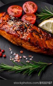 Delicious grilled red salmon fish with sauce, sesame seeds, spices and herbs on a dark concrete background
